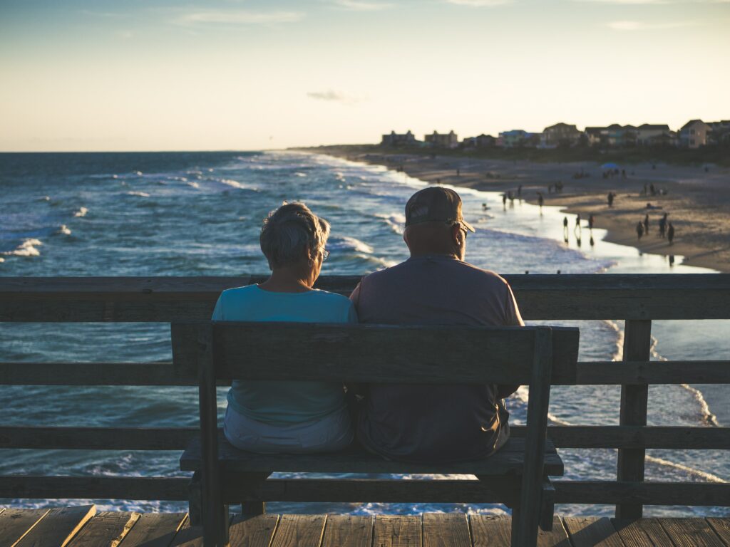 A couple sitting on a bench, overlooking a beach.